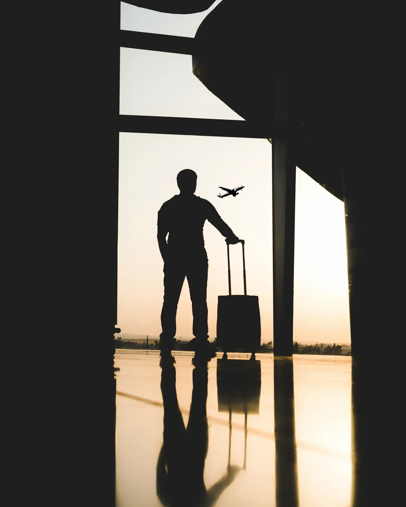 Silhouette of a traveller standing beside rolling luggage near a departure gate