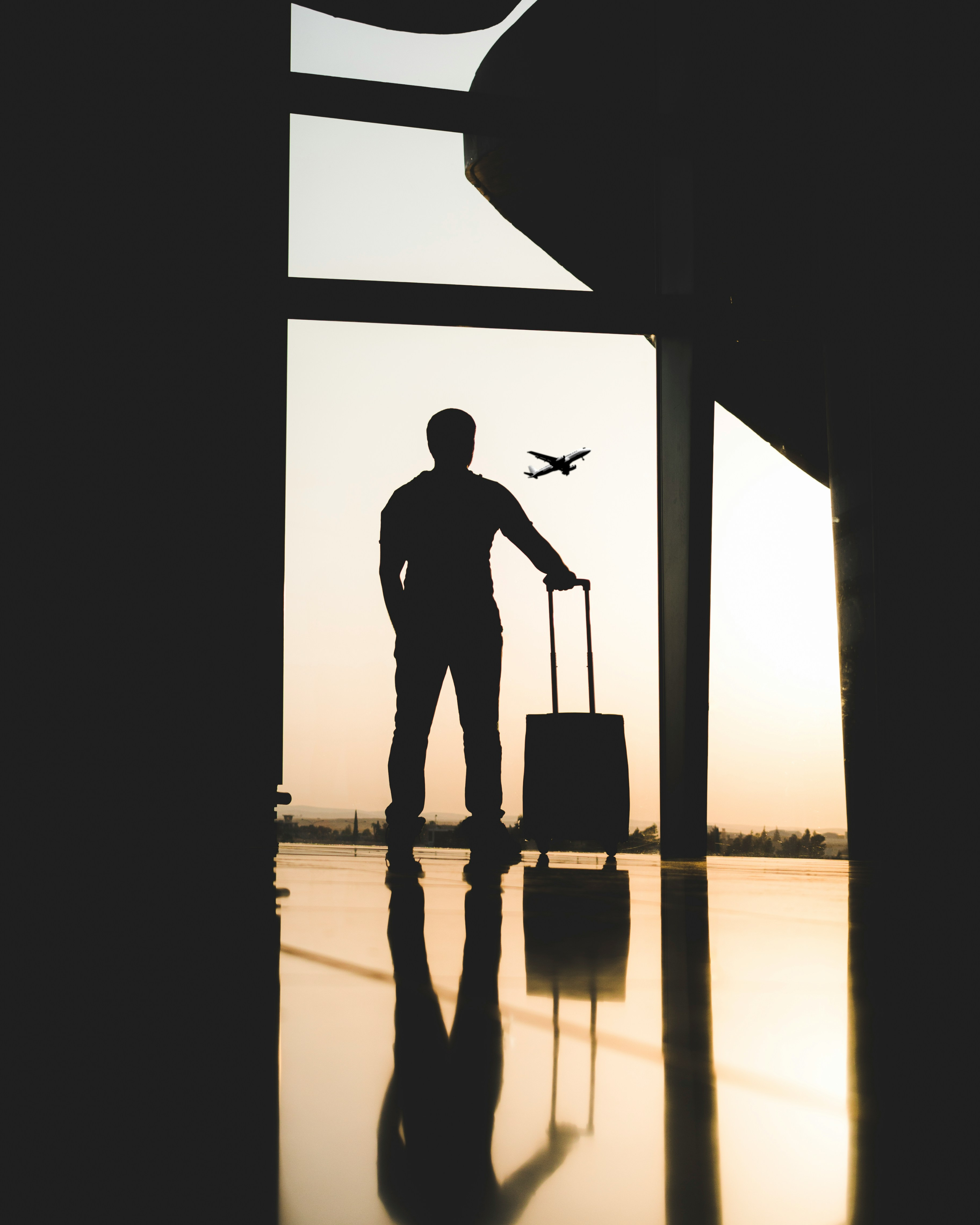 Silhouette of a traveller standing beside rolling luggage near a departure gate
